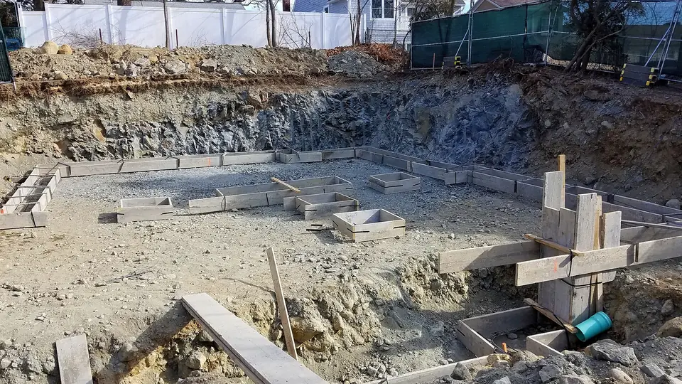 Fondations d'une maison neuve à Arlington, avec semelles en béton coulées en fond de fouille, coffrages en bois et terrain excavé.